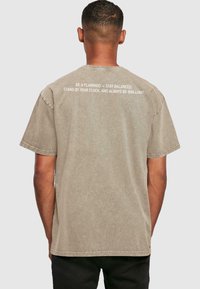 Camiseta de algodón color caqui con cuello redondo, mangas cortas y acabado texturizado. Presenta texto blanco en la parte posterior con una frase motivacional.
