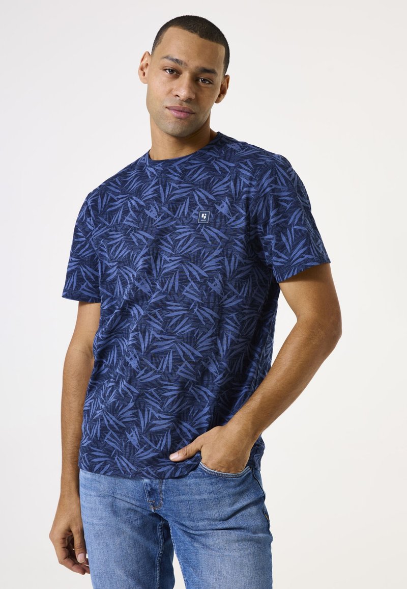 Camiseta de manga corta azul marino con un patrón de hojas, cuello redondo y un pequeño logo en el pecho. Fabricada en una tela ligera y texturizada.