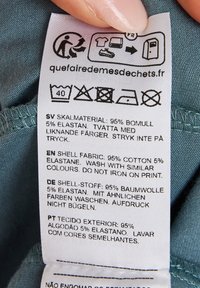 Care label on a teal fabric with text in multiple languages, detailing material composition: 95% cotton, 5% elastane, washing instructions.