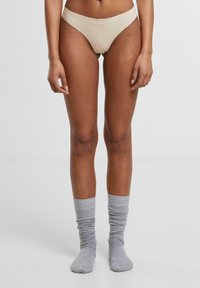 Beige bikiniundertøy med sømløst design, kombinert med løst rullede lysegrå sokker med ribbet tekstur.
