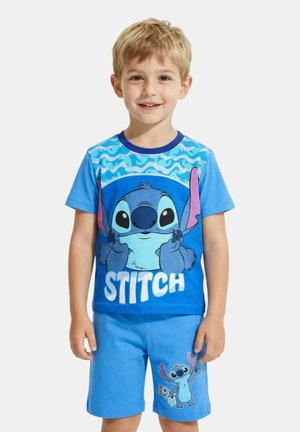 Jeune garçon souriant, portant un short bleu et un t-shirt avec le personnage animé Stitch du film Lilo & Stitch de Disney.