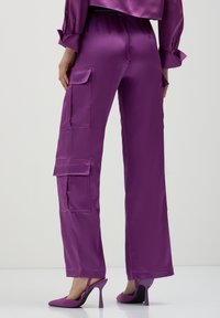 Lila Satin-Cargohosen mit lockerer Passform, ausgestattet mit zwei großen Fronttaschen und Seitennähten, kombiniert mit passenden High Heels.