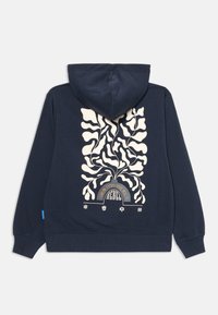 Marineblå hættebluse med cremegul abstrakt plante-design, buet grafik med teksten "Bliv til den vilde rebel", og fire små ikoner langs bunden.