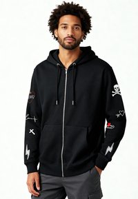 Felpa con cappuccio nera con zip realizzata in misto cotone; presenta patch grafiche tra cui un teschio, un fulmine, un cuore e testo sulle maniche.