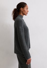 Szary, strukturalny sweter z wysokim kołnierzem i długimi rękawami. Miękki, puszysty materiał, prosty krój i minimalistyczny design. Stylizowany z gładkimi spodniami.