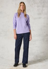 Pull en lilas tricoté avec un col haut et des poignets côtelés, associé à un jean large bleu marine et des bottes noires à semelles épaisses.