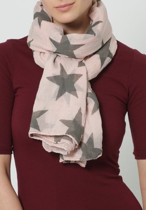 Écharpe rose clair avec de grandes étoiles grises enroulée autour du cou, portée par-dessus un haut bordeaux ajusté.