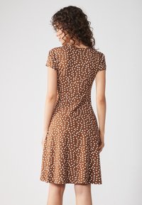 Braunes Kurzarmkleid mit weißen Punkten, taillierter Oberteil, ausgestelltem Rock und rundem Ausschnitt, aus glattem Stoff gefertigt.