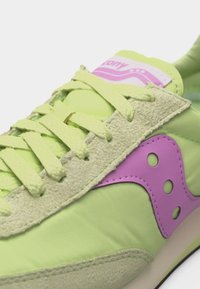 Ανοιχτό πράσινο αθλητικό παπούτσι με υφή από σουέντ, κίτρινα κορδόνια και μοβ διακοσμητικό λογότυπο στο πλάι.