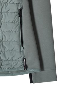 Lysegrå-grøn jakkeærme med quiltede og glatte stofpaneler, sort lynlåslomme og "Cecil Outerwear" label.