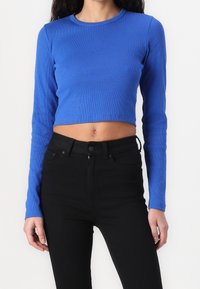 Top corto a maniche lunghe blu a coste con scollatura rotonda, abbinato a jeans neri a vita alta, caratterizzati da una silhouette aderente e un tessuto testurizzato.