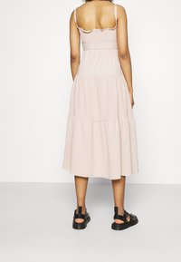 Bledě růžové šaty bez rukávů s nařasenou horní částí, vrstvenou sukní a vroubkovanými detaily. Kombinované s černými sandály s mnoha pásky.