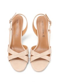Sandalias beige de punta abierta con tiras cruzadas, hebilla en el tobillo y acabado en cuero texturizado, vistas desde arriba.