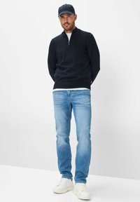 Maglione blu navy con zip al collo, jeans azzurri e sneakers bianche. Il maglione presenta dettagli a coste e un design aderente. Outfit casual.