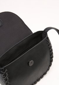 Czarna skórzana torba z wplecionymi akcentami, płaskim dnem, zapięciem na magnes oraz wnętrzem wyłożonym tkaniną z kieszenią na zamek.