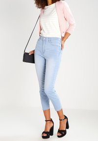 Ljusblå cropped jeans med hög midja, ihop med en vit och gulrandig skjorta och en rosa cardigan. Svarta klacksandaler och en liten svart väska.