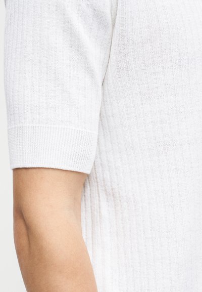 Λευκό πλεκτό τοπ με κοντά μανίκια, ριμπ υφή και αδιάκοπο σχέδιο. Διαθέτει στρογγυλή λαιμόκοψη και μαλακό, ελαφρύ ύφασμα.