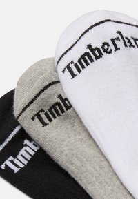 Drei Paare Socken in Schwarz, Grau und Weiß mit dem "Timberland"-Logo, das in Schwarz am Bündchen eingestickt ist. Das Material wirkt weich und dehnbar.