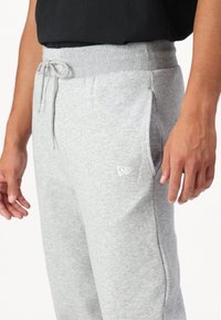 Gray cotton sweatpants with an elastic waistband, drawstring, side pockets, and a small white logo on the left thigh.