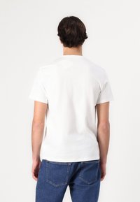 White cotton t-shirt with short sleeves and a crew neckline, paired with blue denim jeans featuring back pockets. Simple, solid color design.