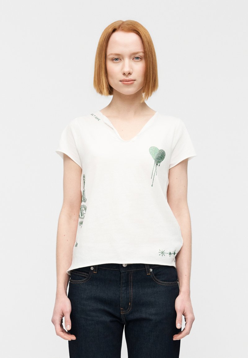 Άσπρο κοντομάνικο μπλουζάκι με λαιμόκοψη σε σχήμα V, με πράσινα γραφικά σχέδια από καρδιές και αστέρια στο μπροστινό μέρος και στον αριστερό ώμο.