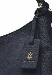 Marinefarbene Lederhandtasche mit strukturierten Oberflächen, goldfarbener Hardware und einem Etikett mit dem Logo "ZL" und "EST 2007."