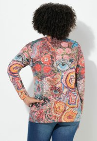 Camiseta de manga larga multicolor con patrones abstractos en rojo, azul y naranja. Tejido suave con escote redondo y silueta ajustada.