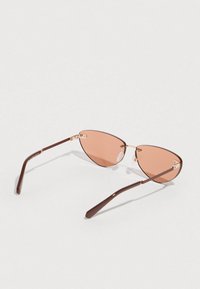 Rjave kovinske sončna očala s cat-eye obliko in roza odtenki leč. Ponašajo se z zlati poudarki in prozornimi oporniki za nos za boljše udobje.