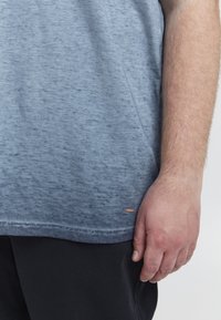 Lys blå crew neck t-shirt med en subtil tekstur, der har en cropped pasform og et lille mærke i kanten. Båret sammen med sorte shorts.