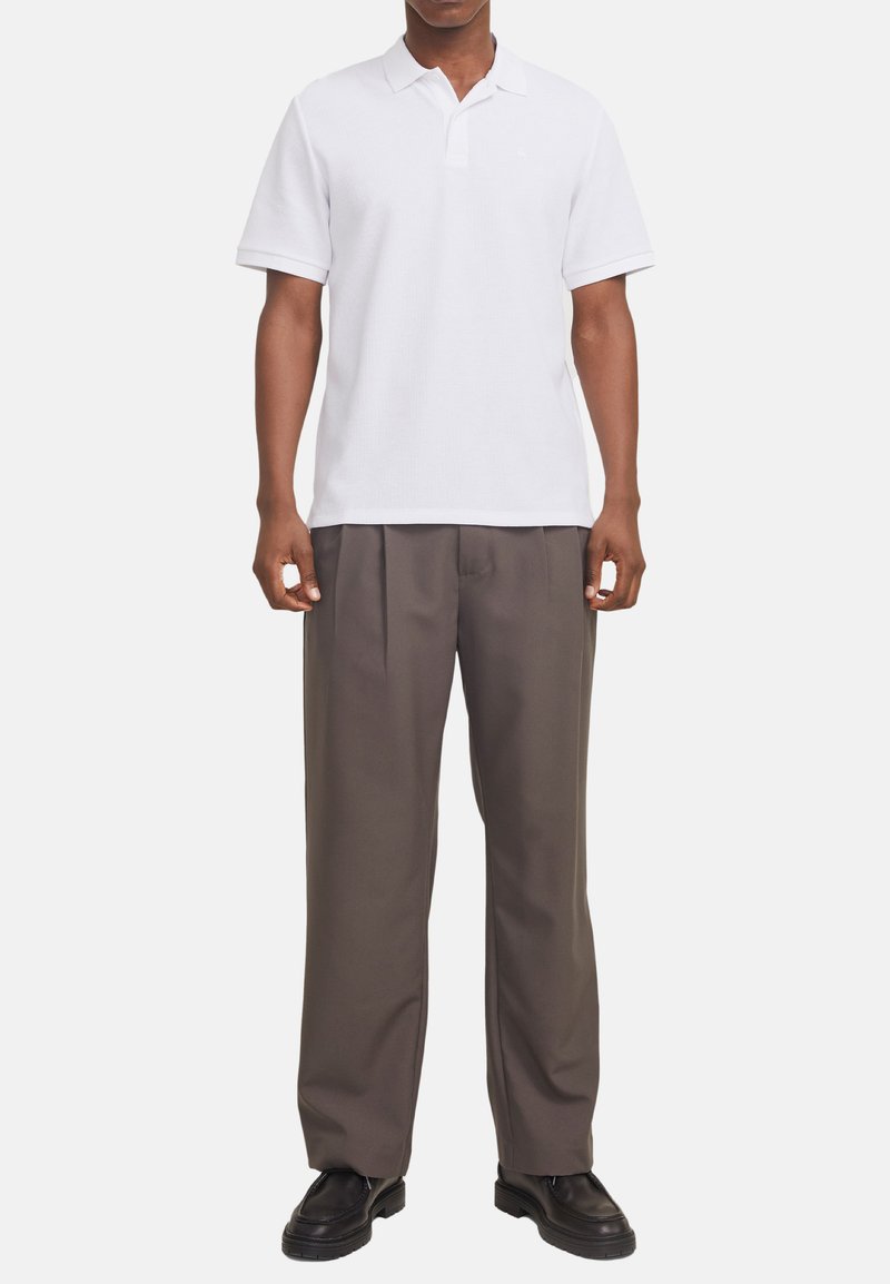 Hvid kortærmet polo t-shirt med en tekstureret overflade, parret med brune plisserede bukser og sorte slip-on sko.