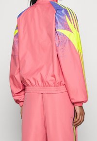 Rosa vindjacka med elastiska muddar och resår i midjan, med blå och neon gula accenter samt ett stänkigt mönster på ärmarna.