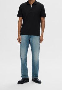 Svart kortärmad pikétröja med dragkedja vid kragen, i kombination med ljusblå rakbenjeans och svarta skor. Slät tyg med avslappnad passform.