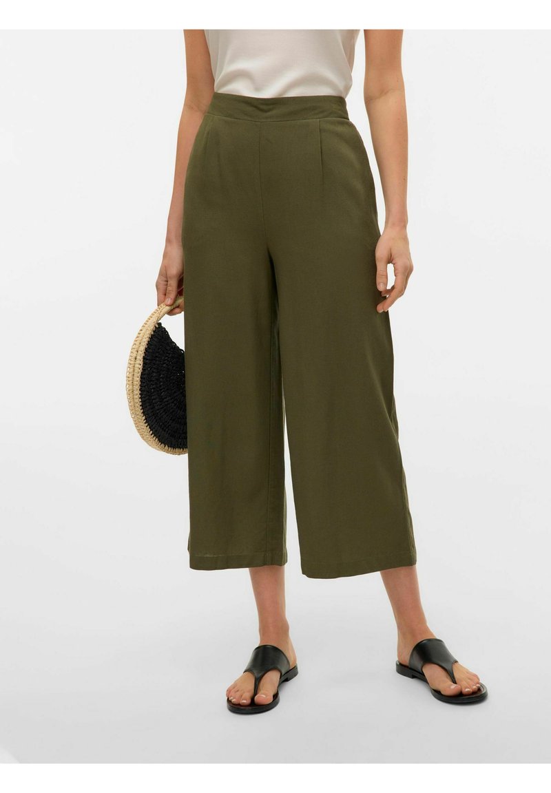 Pantalons larges en vert olive en tissu léger, dotés d'une taille haute, de plis et d'un ourlet propre. Associés à des sandales plates noires et à un sac tissé.