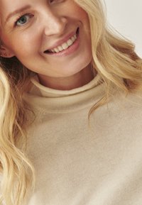 Heledbeez värvi kootud sviiter kõrge ja keeratud kaelusega, millel on sile tekstuur ning pehme ja soe välimus. Silmapaistmatu õmbluse detail on nähtav.