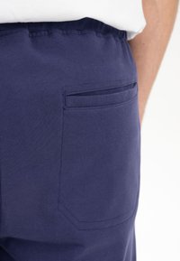 Marineblaue Baumwollhose mit einer Seitentasche, die eine glatte Textur und einen taillierten Bund aufweist. Minimalistisches Design ohne sichtbare Verzierungen.
