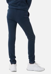 Marineblå fleece-joggingbukser med ribbede manchetter, slim fit-design og sidelommer, parret med hvide sportssko.