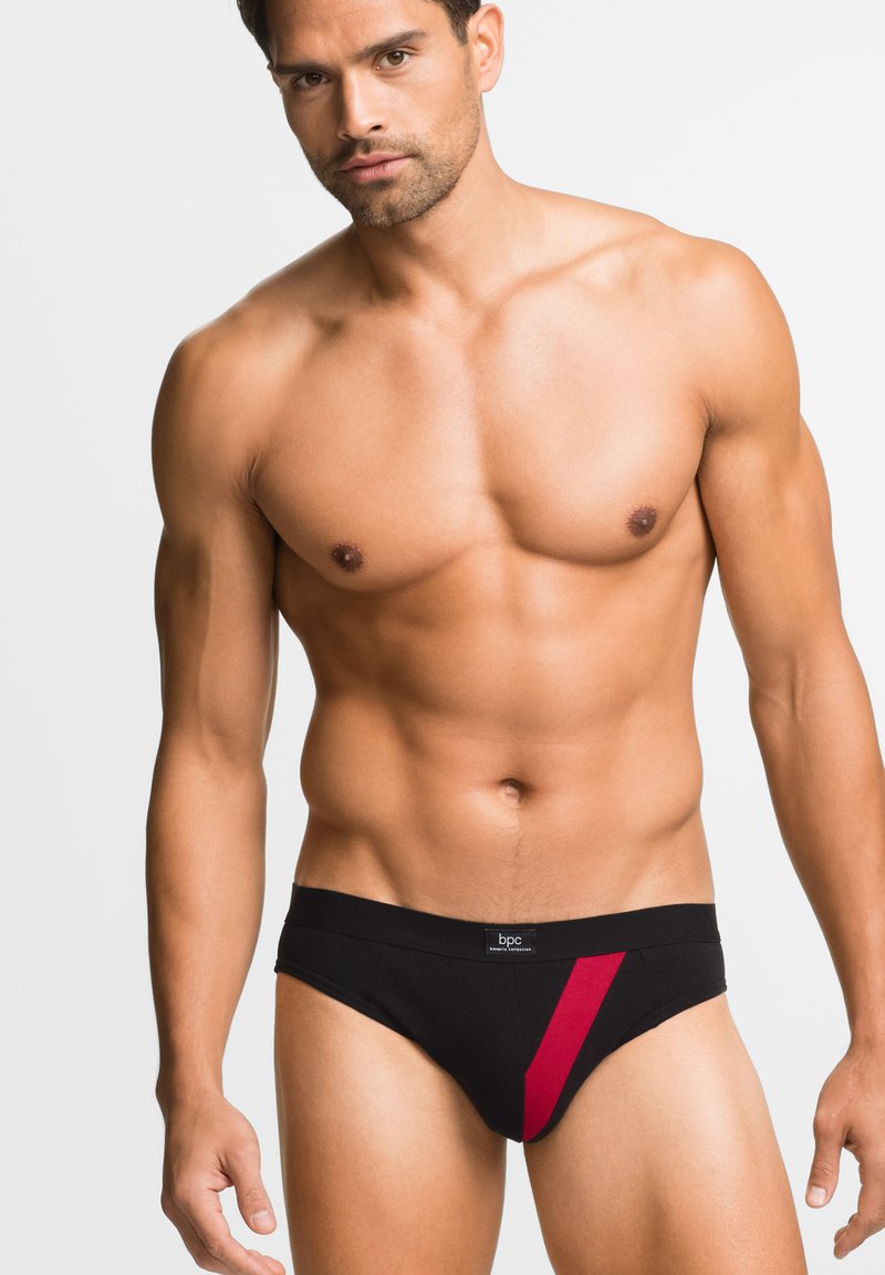Slip nero con una striscia diagonale rossa, dotato di una cintura morbida e di un tessuto liscio. Progettato per una vestibilità aderente e una copertura minima.