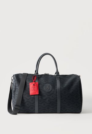 Sac polochon noir avec motif répétitif du logo de Paris, deux poignées supérieures, bandoulière réglable et étiquette à bagages rouge attachée à la poignée.