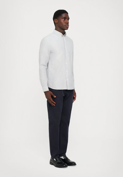Camicia button-up a righe azzurre e bianche, abbinata a pantaloni blu scuro e scarpe eleganti nere. Tessuto morbido, vestibilità sartoriale.