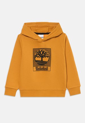 Sweatshirt à capuche jaune en tissu doux, présentant un graphique noir avec un motif d'arbre et le texte "Timberland" en dessous. Poignets et ourlet côtelés.