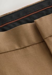 Tissu marron texturé avec une surface lisse, doté d'une doublure intérieure noire et d'une couture de contraste brun le long du bord supérieur.