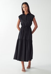 Must mustriga ilma varrukateline kleit, millel on nuppe kinni pandud esikülg, vöökohal kokku tõmmatud ja kihiline seelik. Valmistatud kergest kangast, millel on sile tekstuur.