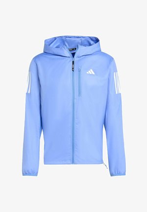 Chaqueta ligera azul clara con capucha, cierre frontal de cremallera y puños elásticos. Presenta el logo blanco de Adidas y acentos a rayas en las mangas.