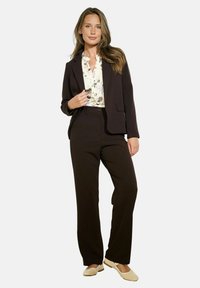 Blazer nero su misura con pantaloni abbinati, abbinato a una blusa floreale. Tessuto liscio, design strutturato e ballerine chiare.