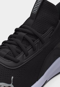 Αθλητικό παπούτσι Puma σε μαύρο χρώμα με επάνω μέρος από διχτυωτό υλικό, μαύρα κορδόνια και λευκή σόλα, με το λογότυπο Puma στην πλευρά και ετικέτα με το σήμα στην γλώσσα του παπουτσιού.