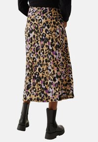 Plissé midi-rok in een luipaardprint met tinten beige, zwart en paars, gedragen met zwarte enkellaarsjes.