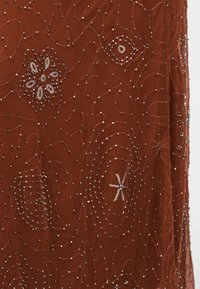 Ύφασμα σε σκουριά απόχρωση με περίπλοκη διακόσμηση από χάντρες που σχηματίζουν ανθικά και αφηρημένα κυκλικά μοτίβα, δημιουργώντας μια υφή και διακοσμητική επιφάνεια.