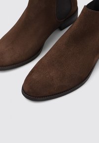 Bottines en suède marron avec un bout pointu, des panneaux latéraux élastiques et un talon solide noir bas. Texture lisse et design minimaliste.
