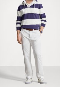 Sudadera a rayas en azul marino y blanco con un bolsillo delantero, combinada con pantalones blancos y zapatillas claras. El conjunto presenta un ajuste casual y relajado.