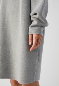 Main reposant à côté d'une personne portant une robe en maille à manches longues gris clair avec des poignets côtelés.